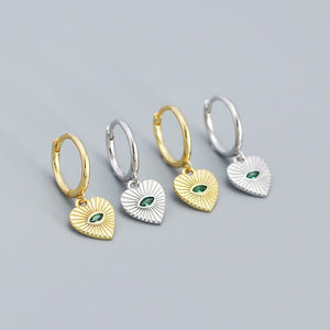 Four pairs of hoop earrings with heart-shaped charms on a gray background