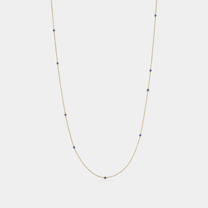 Gold necklace with small blue beads on a light gray background