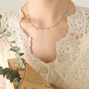 Close-up of a person wearing a lace garment with a necklace, holding a book and plant.