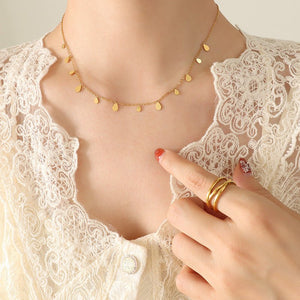 Gold necklace on a person wearing a lace top with a hand touching the necklace.