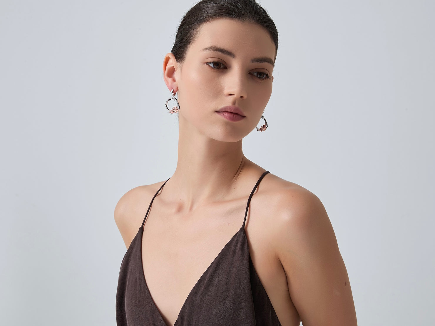 Woman wearing a brown dress with thin straps against a light gray background