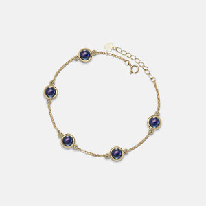 Gold bracelet with blue gemstones on a light gray background