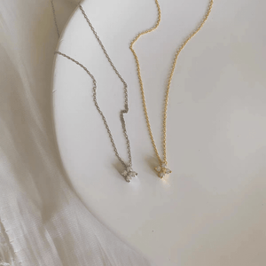 Two necklaces, one gold and one silver, on a white fabric background.