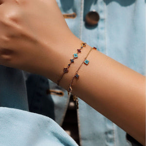 Close-up of a person's wrist wearing a delicate bracelet with colorful stones against a denim background.