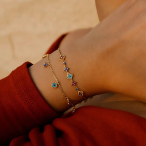Close-up of a person's wrist wearing a gold bracelet with colorful stones on a beige background.