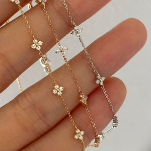 Two delicate gold necklaces with floral pendants on a hand against a neutral background