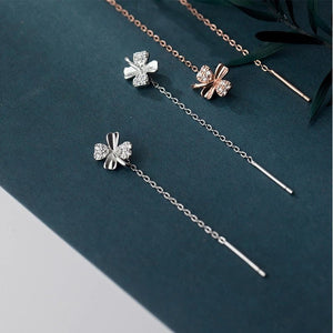 Pair of silver floral earrings with chain extensions on a dark green surface.