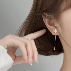 Close-up of a person wearing a delicate earring with a hand pointing to it.
