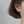 Close-up of a person wearing a silver four-leaf clover earring on a neutral background