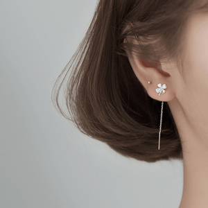 Close-up of a person wearing a silver four-leaf clover earring on a neutral background