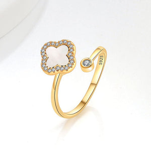 A collection of four leaf clover-shaped fidget spinner rings with various colored gemstones in silver and gold finishes.