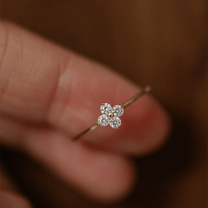 Gold ring with a diamond flower design held between fingers against a blurred background