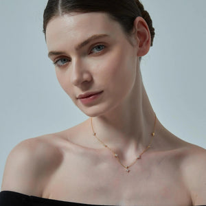 Woman wearing a delicate gold necklace against a plain background