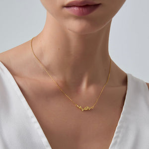 Gold necklace on a person wearing a white top against a neutral background