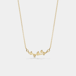 Gold necklace with leaf-like pendant on a light gray background