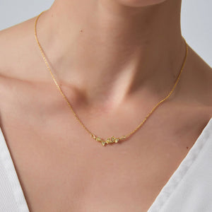 Gold necklace with small green stones worn by a person against a neutral background