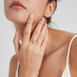 Woman wearing a gold spinner ring with blue evil eye design and small diamond on a light gray background