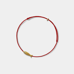 A gold fish-shaped charm on a braided rope anklet against a white background