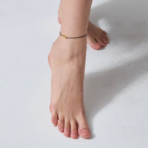 Close-up of a foot wearing a gold anklet on a light background