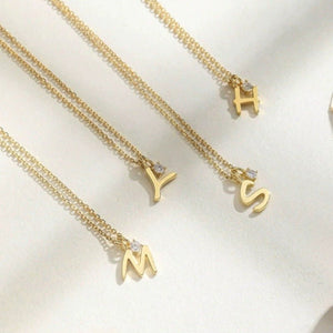 Gold necklaces with letter pendants on a light background