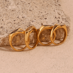 Four gold rings arranged in a row on a textured stone surface