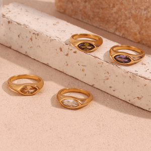 Four gold rings with gemstones on a textured beige surface
