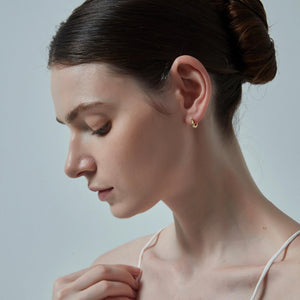 Close-up of a woman wearing a gold earring against a neutral background
