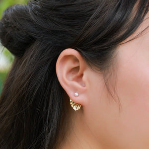 Close-up of an ear with a gold earring and pearl stud, hair styled in a bun.