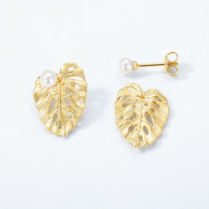 Gold leaf-shaped earrings with pearl centers on a light gray background