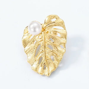 Gold leaf-shaped brooch with a pearl on a white background