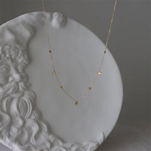 A gold star charm layering necklace laid out on a white dish with ornate patterns, showcasing its delicate chain and multiple star charms.