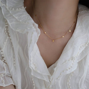 Gold necklace with star-shaped pendants on a person wearing a white blouse.