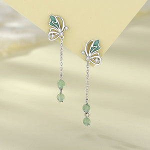 Butterfly-shaped earrings with green beads on a reflective surface