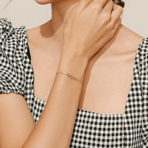 Person wearing a gold bracelet with green stones on a checkered sleeve.