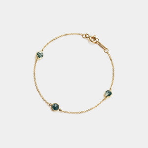 Gold bracelet with green gemstones on a white background