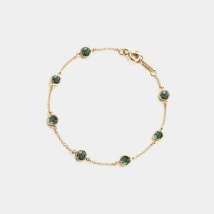 Gold bracelet with green gemstones on a light gray background