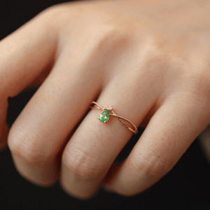 Gold ring with a green gemstone on a finger against a dark background