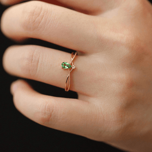 Gold ring with a green gemstone on a person's finger against a dark background