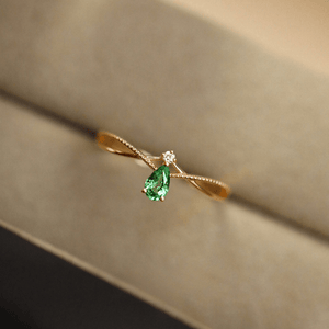 Gold ring with a green gemstone on a beige surface