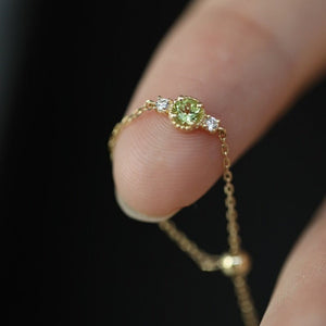 Gold ring with a green gemstone on a finger against a dark background