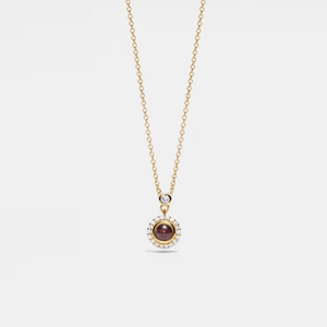 Gold necklace with a pendant featuring a red gemstone on a light gray background