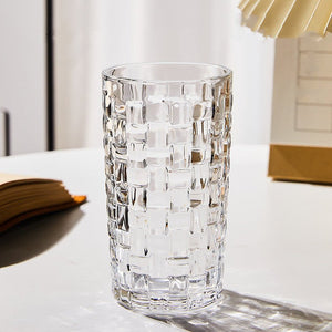 A multicolored hand-painted grid woven drinking glass with a geometric pattern, displayed on a table.