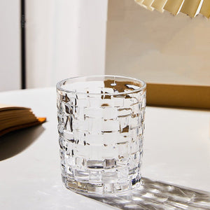 A multicolored hand-painted grid woven drinking glass with a geometric pattern, displayed on a table.