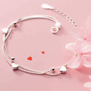 Silver bracelet with heart-shaped charms on a pink background