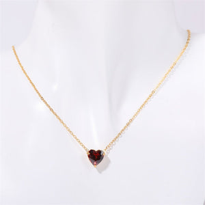 Gold necklace with a heart-shaped red gemstone on a white background