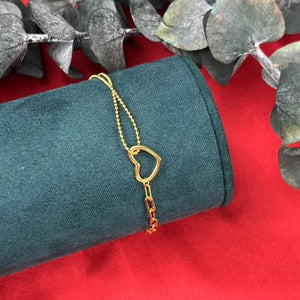 Gold bracelet on a green velvet cushion with a red background and green leaves.