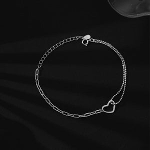 A silver bracelet featuring a heart-shaped charm and two interlinked chains on a black background.