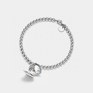 Silver beaded bracelet with a heart-shaped locket charm shown open, featuring a smooth polished exterior and a photo insert inside, displayed on a light gray background