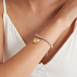 A model wearing a silver beaded bracelet with a gold heart-shaped locket charm