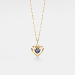 Gold heart-shaped necklace with a blue gemstone on a white background
